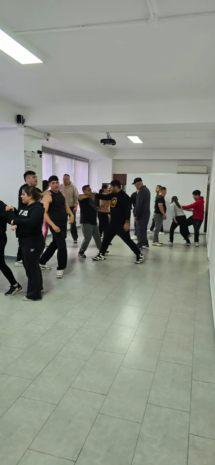Grupo practica desplazamientos y posiciones de defensa en la sala de entrenamiento.