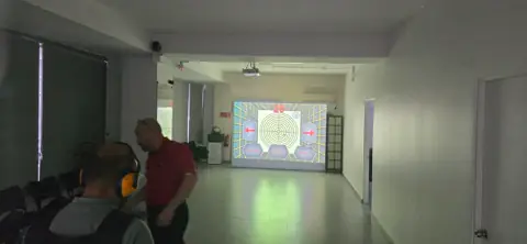 Alumno con protección auditiva y su instructor frente a la pantalla del polígono virtual.