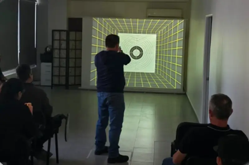 Alumno apunta a la diana proyectada en la pared del polígono virtual de ZCAP mientras otros observan.