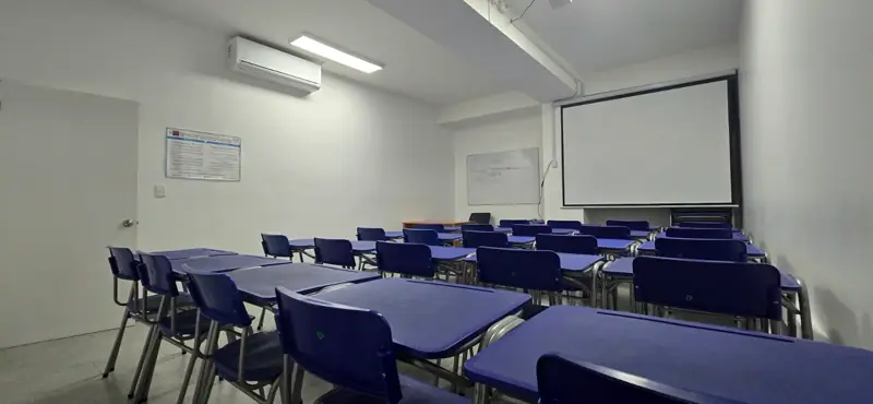 Sala de clases de ZCAP con pupitres azules y pantalla de proyección.