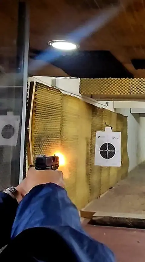 Disparo de pistola visto desde la mano del tirador, con el fogonazo frente a la diana en el polígono techado.