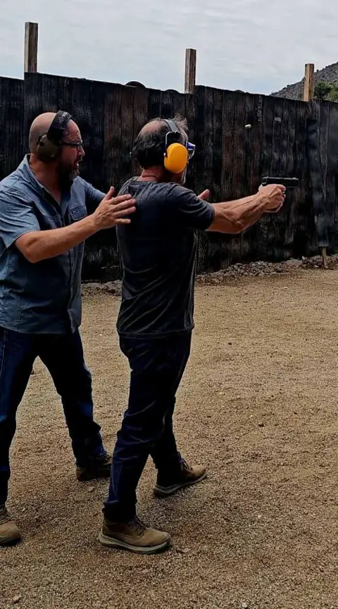 Instructor corrige la postura de un alumno que dispara una pistola en el polígono exterior.